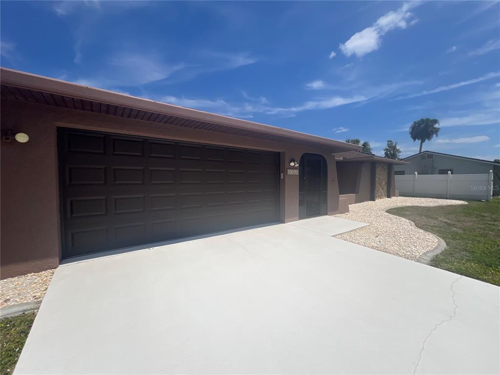 A brown house exterior features a dark garage door, a concrete driveway, and a gated entryway — 21212 BURKHART DRIVE, PORT CHARLOTTE, FL