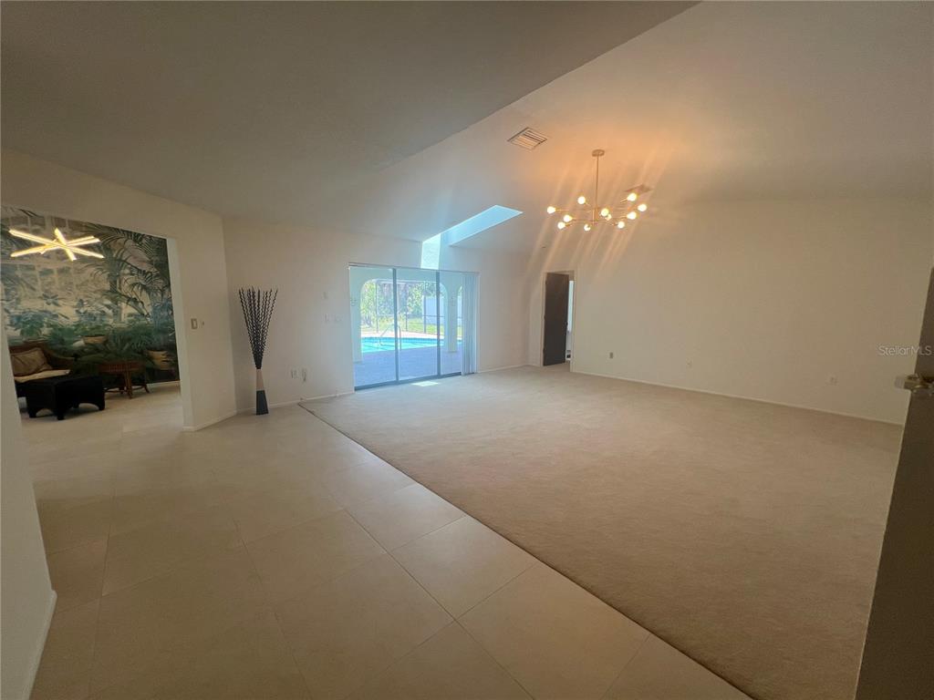 A spacious living room features beige carpeting, tile flooring, a chandelier, and sliding glass doors — 21212 BURKHART DRIVE, PORT CHARLOTTE, FL