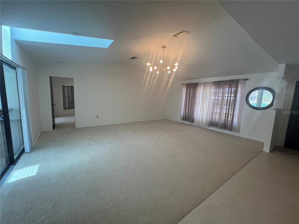 A spacious living room features beige carpeting, a vaulted ceiling, a chandelier, and a skylight — 21212 BURKHART DRIVE, PORT CHARLOTTE, FL