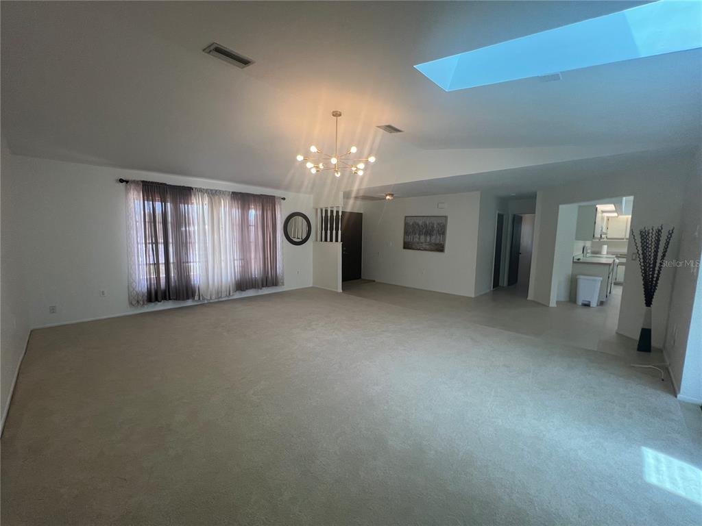 A spacious living room features beige carpeting, a vaulted ceiling with a skylight, and chandelier — 21212 BURKHART DRIVE, PORT CHARLOTTE, FL