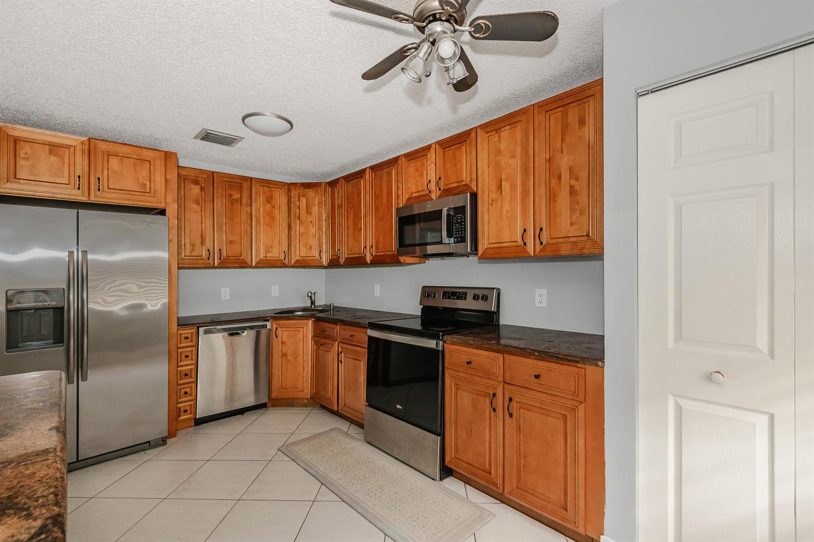 A kitchen features wood cabinets, stainless steel appliances, dark countertops, and light tile flooring — 161 Meadows Drive # 161, Boynton Beach FL 33436, BOYNTON BEACH, FL
