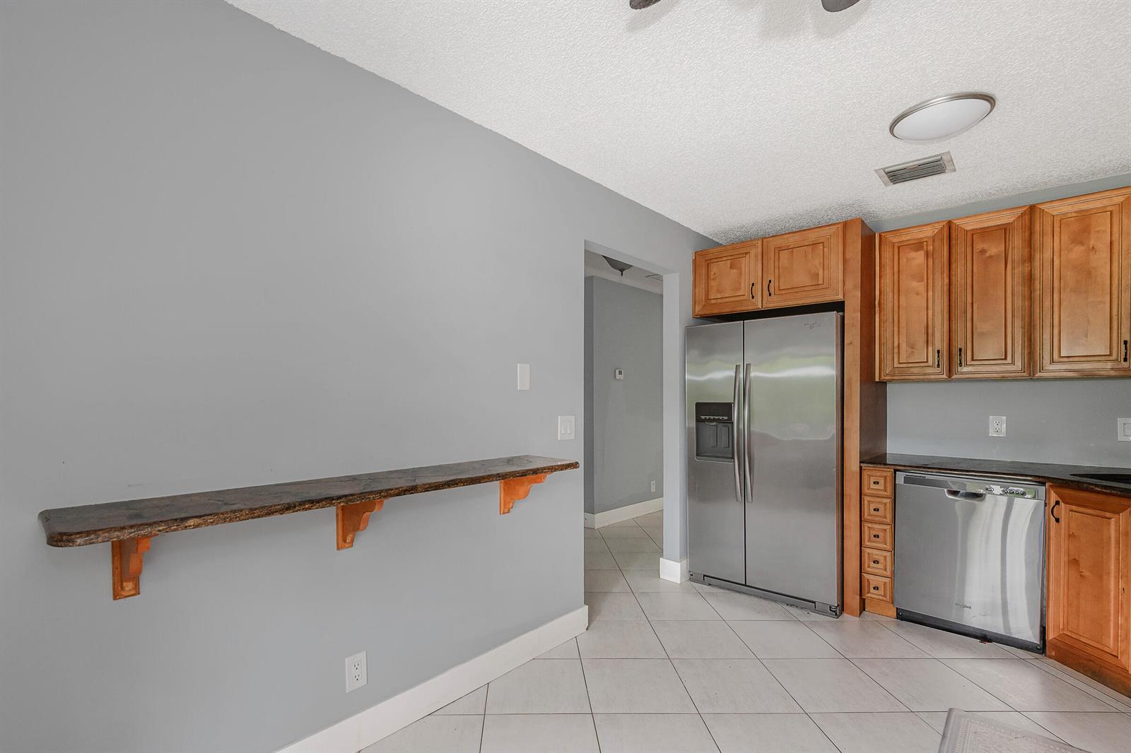 A kitchen features a wooden wall-mounted shelf, stainless steel appliances, and light-colored tile flooring — 161 Meadows Drive # 161, Boynton Beach FL 33436, BOYNTON BEACH, FL