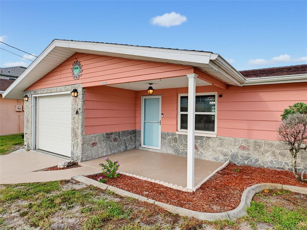 A peach-colored house features a stone facade, a covered porch, and a single-car garage — 13530 MARIA DRIVE, HUDSON, FL