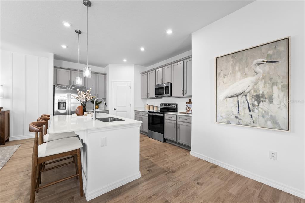A modern kitchen features gray cabinets, a white island with seating, and a large bird painting — 806 CASTLEFORD AVENUE NE, PALM BAY, FL