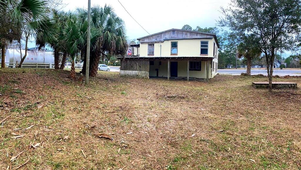 A two-story, light-yellow house with a covered porch stands behind a grassy yard — 16500 S US HIGHWAY 19, SALEM, FL