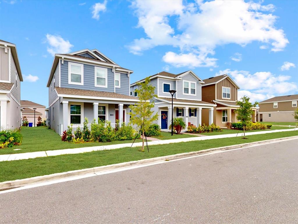 A street-level view of three suburban houses with blue and brown siding under a cloudy sky — 2538 PEACE OF MIND AVENUE, KISSIMMEE, FL