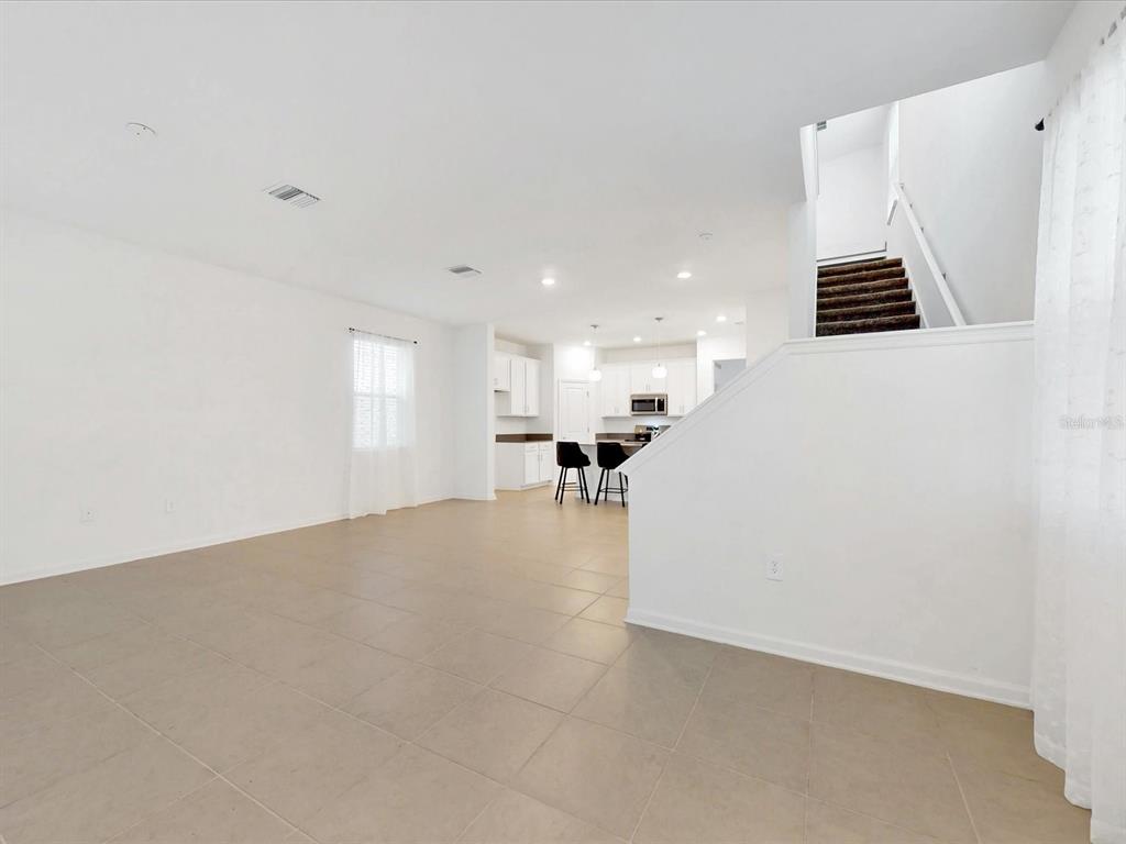 An open-concept living area with tile flooring, white walls, and a staircase leading upstairs — 2538 PEACE OF MIND AVENUE, KISSIMMEE, FL