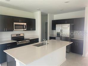 A modern kitchen features dark cabinets, stainless steel appliances, and a white quartz island countertop — 1738 FOREMAN ROAD, EAGLE LAKE, FL