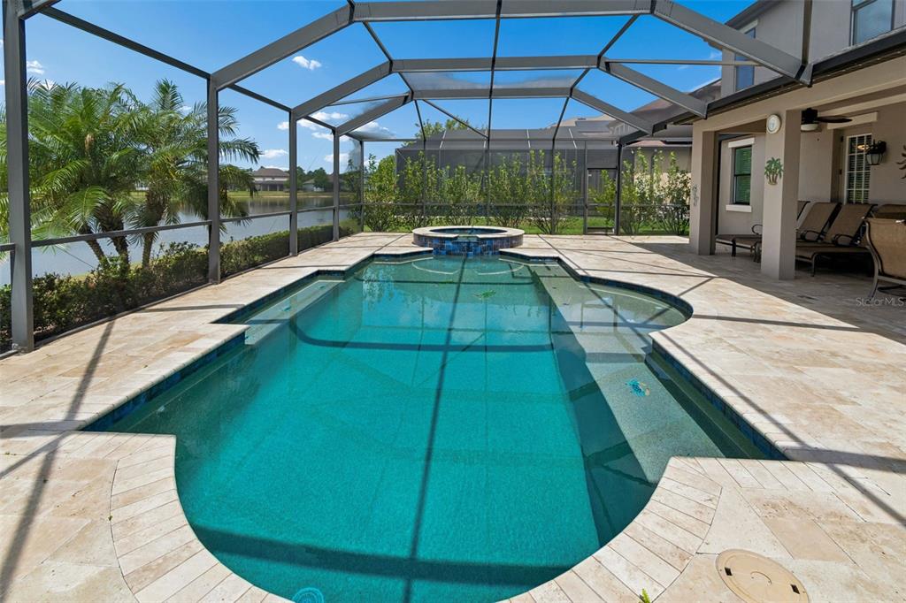 A screened-in swimming pool and spa with a stone patio overlooking a lake — 13218 BATTEN LANE, ODESSA, FL