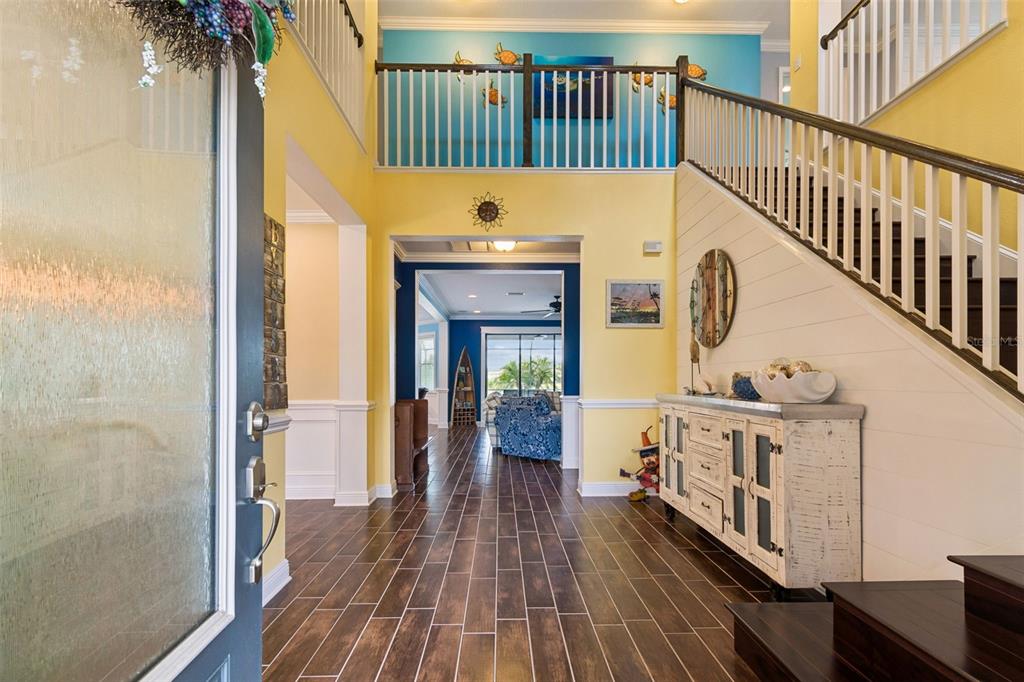 A bright foyer features yellow walls, dark wood-look tile floors, and a staircase with white railings — 13218 BATTEN LANE, ODESSA, FL