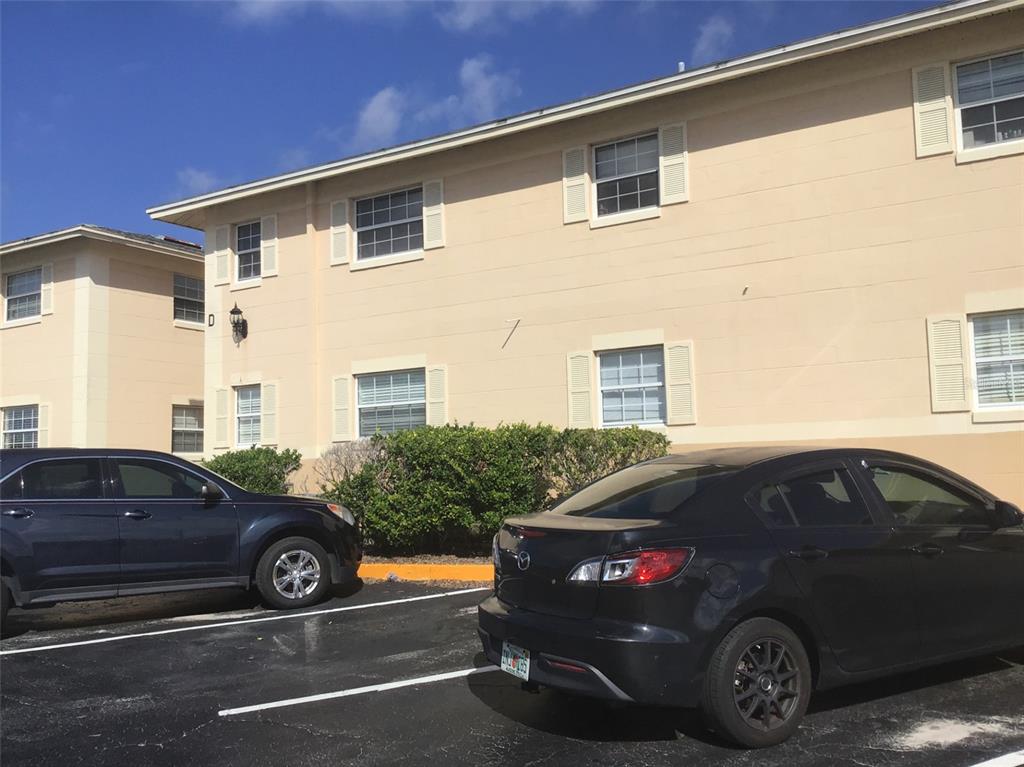 A two-story tan apartment building exterior with two cars parked in the foreground — 1400 EUDORA ROAD UNIT D-38, MOUNT DORA, FL