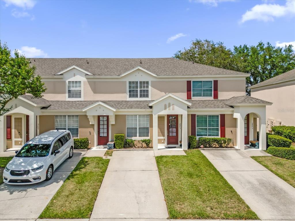 A row of three two-story townhomes with beige stucco siding and individual concrete driveways — 2403 SILVER PALM DRIVE, KISSIMMEE, FL