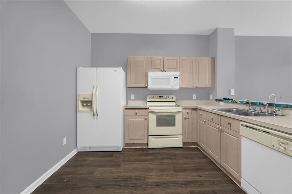 A kitchen features light wood cabinets, white appliances, and dark wood-look flooring — 2403 SILVER PALM DRIVE, KISSIMMEE, FL
