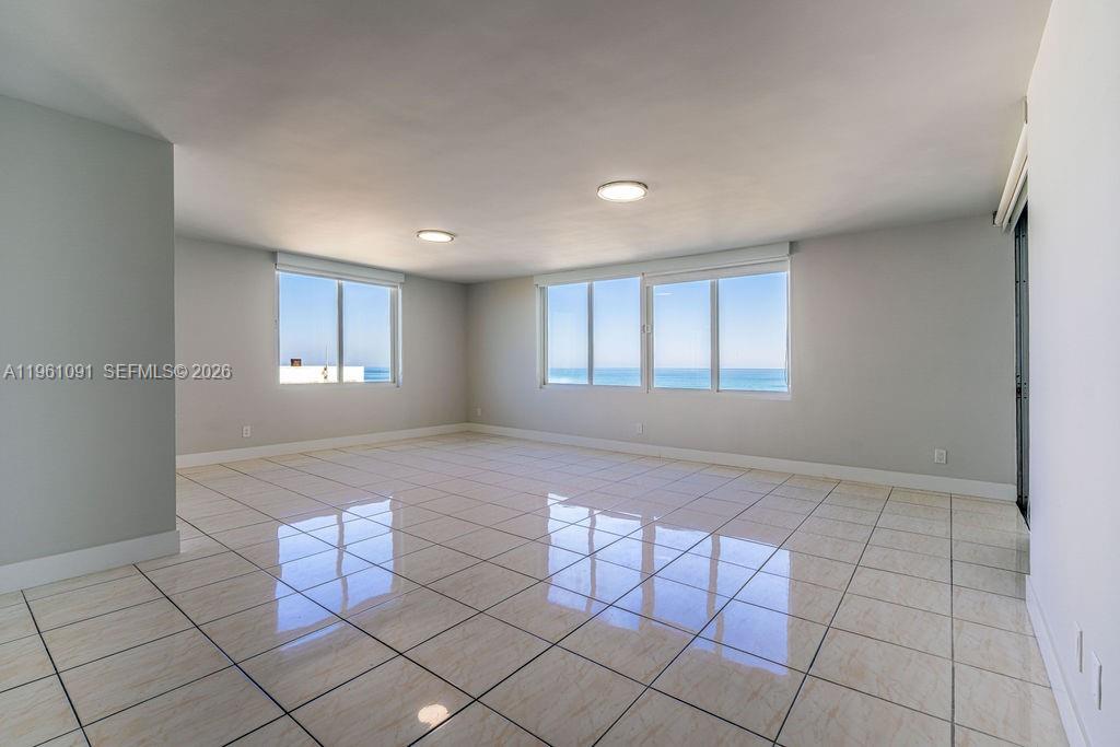 An empty room features light-colored tile flooring, white walls, and large windows overlooking the ocean — 5401 Collins Ave # 919, Miami Beach FL 33140, MIAMI BEACH, FL