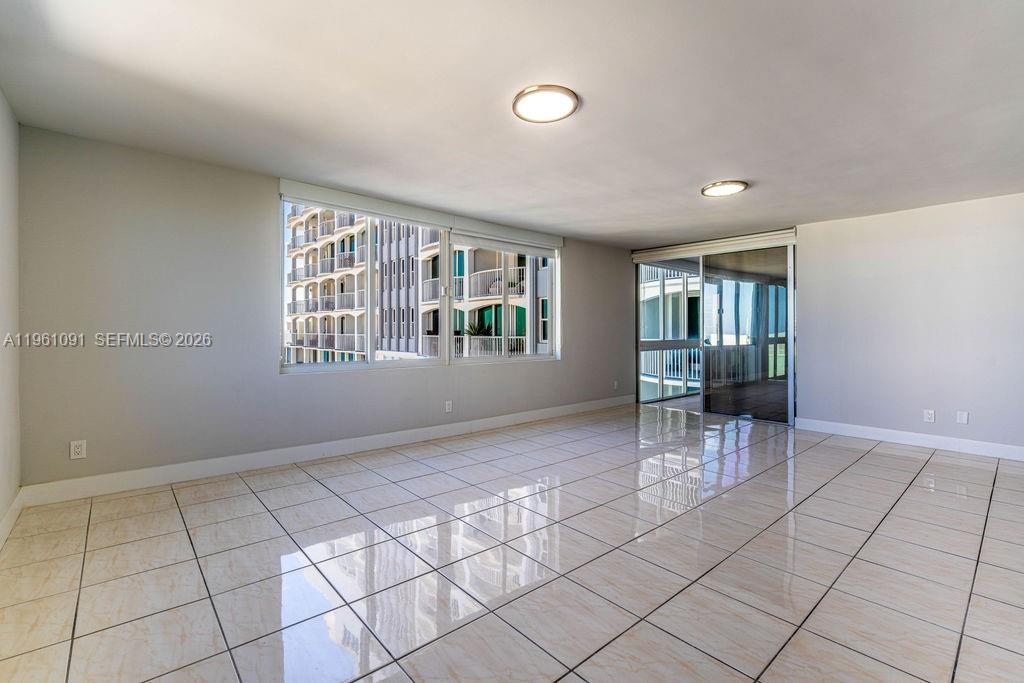An empty room features light-colored tile flooring, white walls, and large windows overlooking a building — 5401 Collins Ave # 919, Miami Beach FL 33140, MIAMI BEACH, FL
