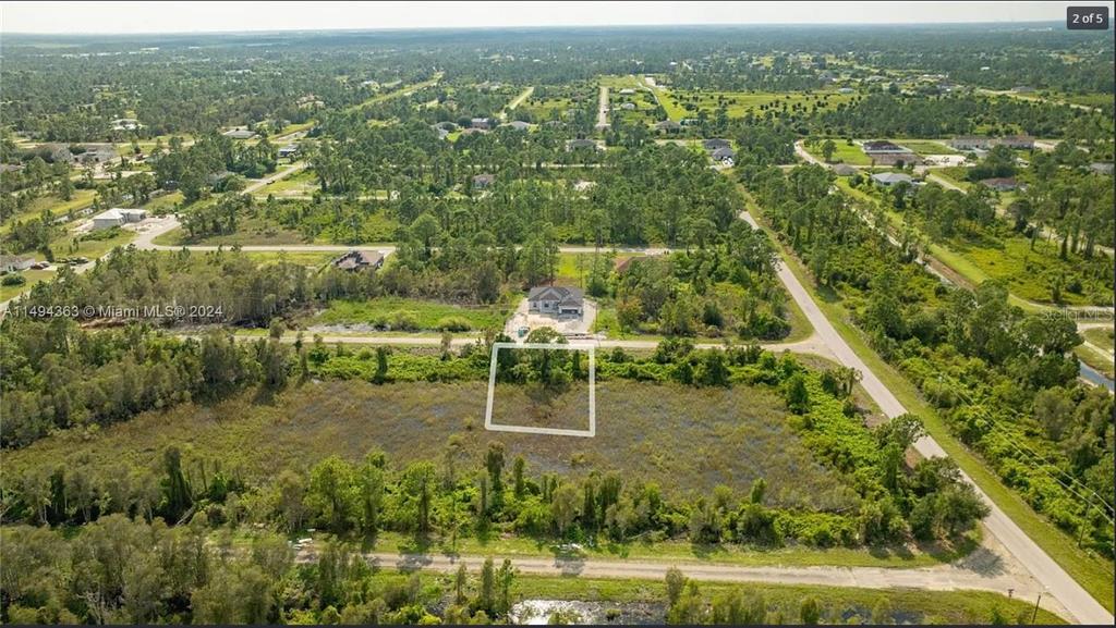 An aerial view shows a vacant, rectangular lot outlined in white near a residential house — 853 BELDEN AVENUE, LEHIGH ACRES, FL