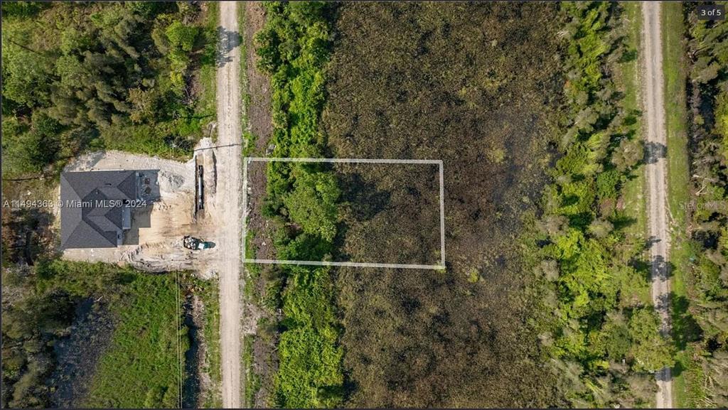 An aerial view shows a rectangular plot of land outlined in white next to a house — 853 BELDEN AVENUE, LEHIGH ACRES, FL