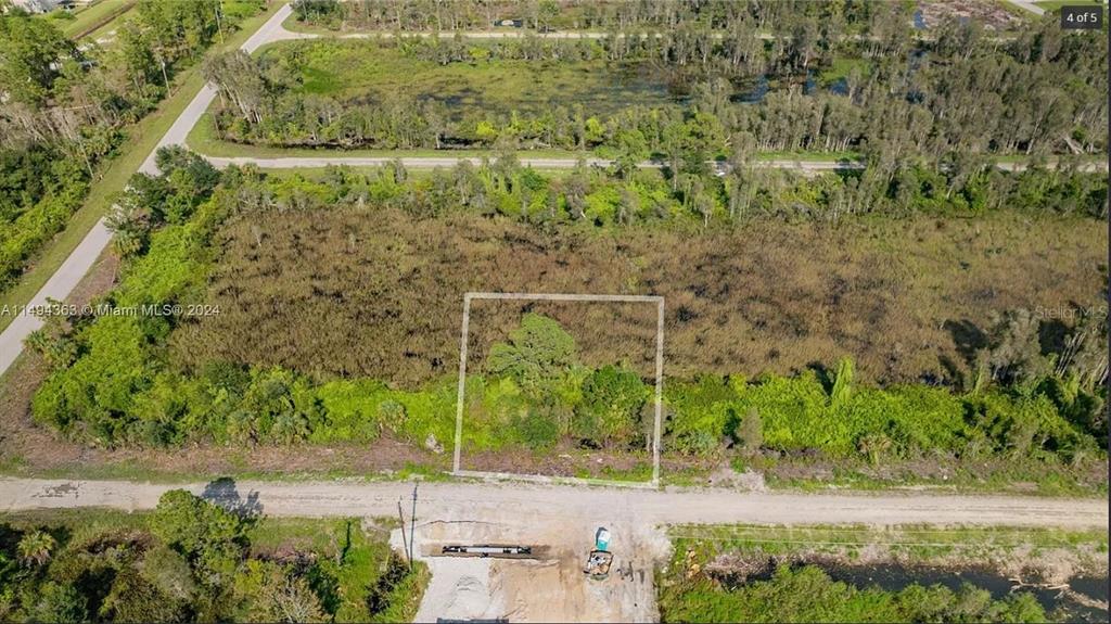 An aerial view shows a rectangular plot of land outlined in white amidst dense vegetation — 853 BELDEN AVENUE, LEHIGH ACRES, FL