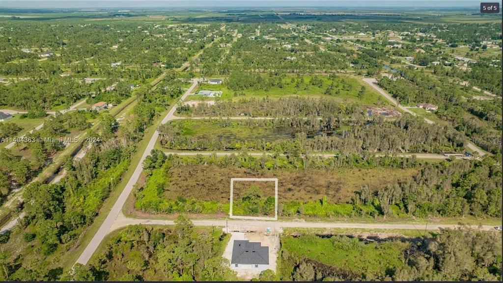 An aerial view shows a vacant rectangular lot outlined in white near a paved road — 853 BELDEN AVENUE, LEHIGH ACRES, FL
