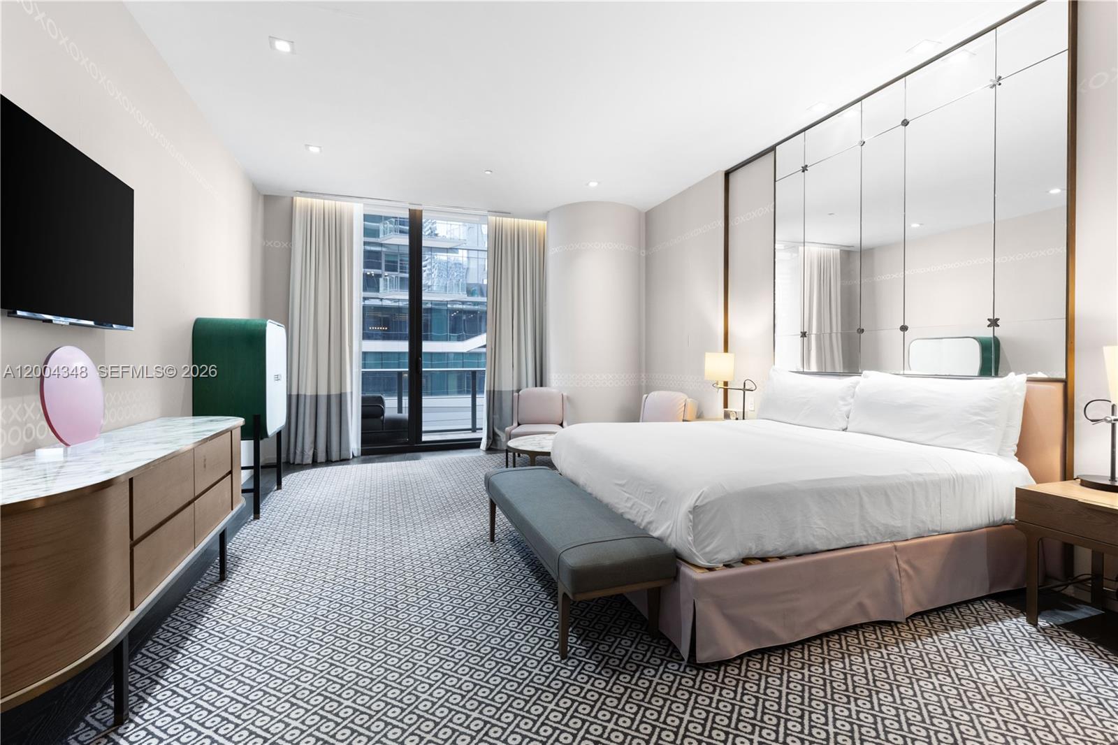 A modern bedroom features a king bed, mirrored wall panels, and a balcony with city views — 801 Miami Ave # 709, Miami FL 33130, MIAMI, FL