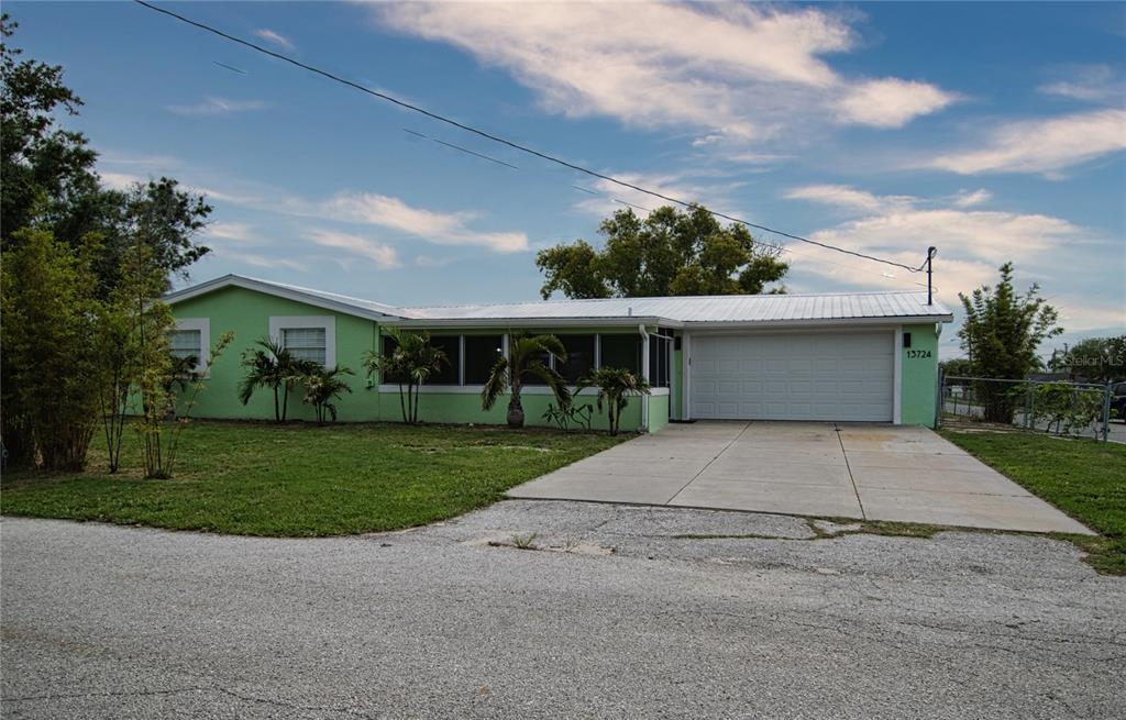 A light green single-story house with a white garage door and a metal roof — 13724 COX AVENUE, HUDSON, FL