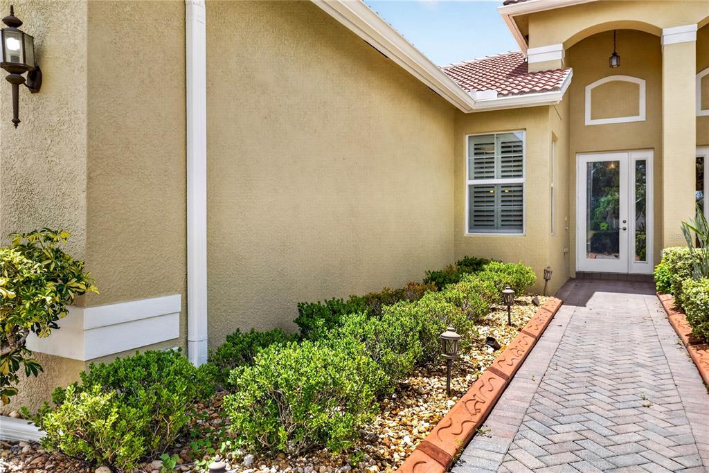 A paved walkway leads to the front entrance of a tan stucco house with landscaping — 16141 AMETHYST KEY DRIVE, WIMAUMA, FL