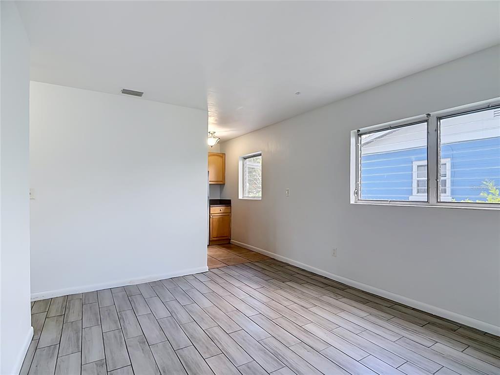 An interior view shows a room with light wood-look tile flooring and a kitchen beyond — 1025 S CENTRAL AVENUE, LAKELAND, FL