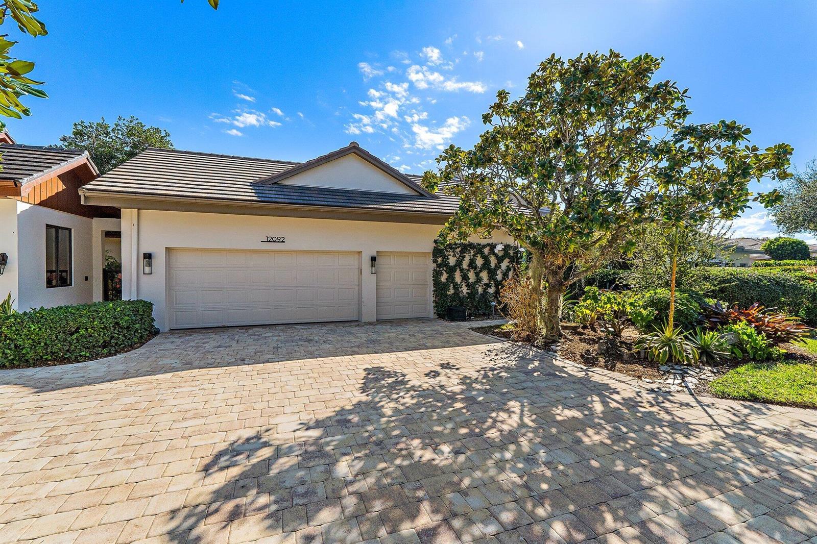 A beige house with a two-car garage and a paved driveway under a blue sky — 12092 SE Birkdale Run, Jupiter FL 33469, JUPITER, FL