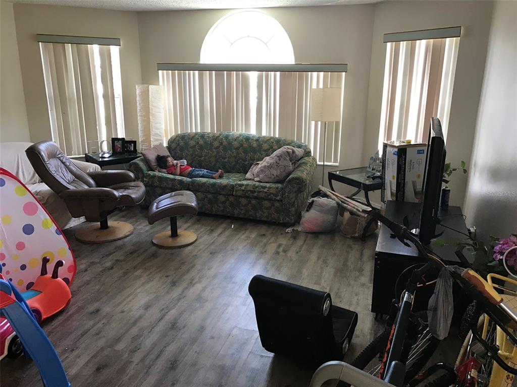 A living room features wood-look flooring, a floral sofa, a recliner, and large windows — 2468 SWEETWATER CLUB CIRCLE UNIT 111, KISSIMMEE, FL