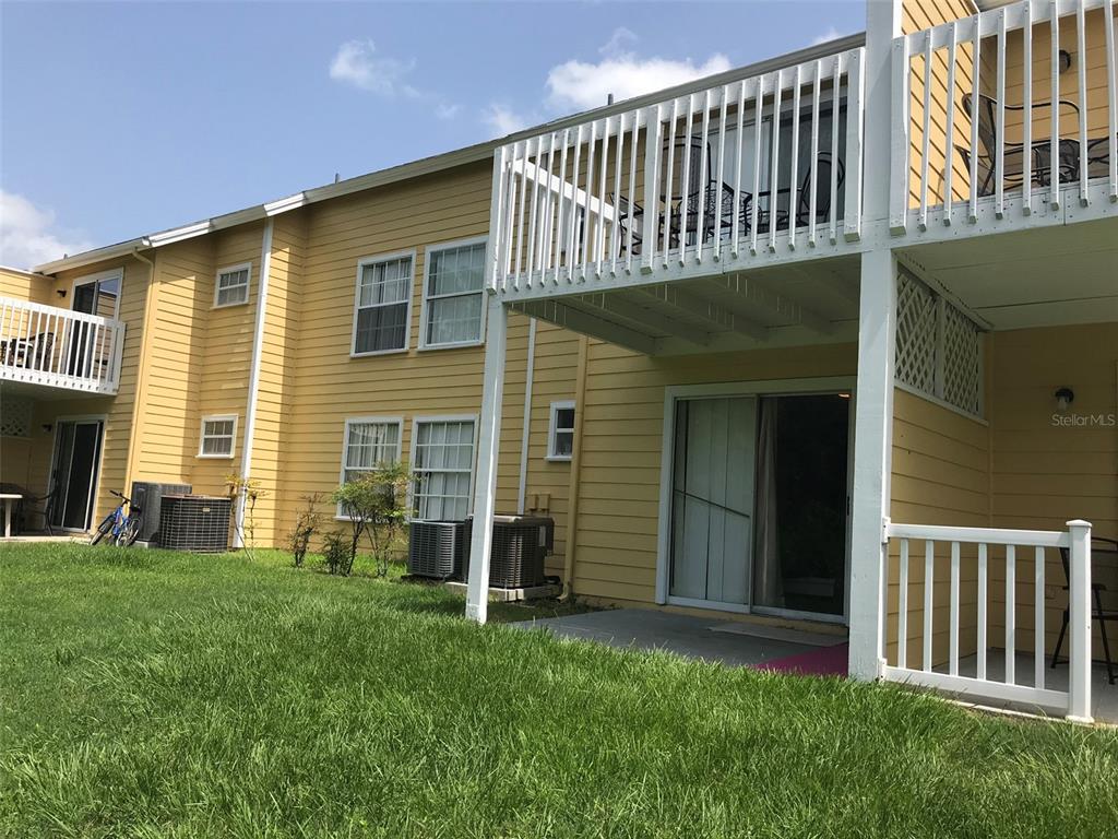 A yellow two-story apartment building features white balconies, sliding glass doors, and a grassy lawn — 2468 SWEETWATER CLUB CIRCLE UNIT 111, KISSIMMEE, FL