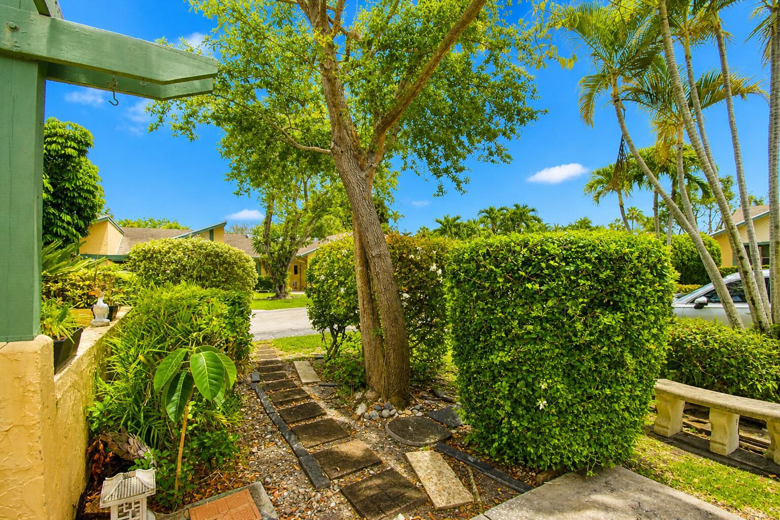 A stone path leads through a lush garden with trimmed hedges and a large tree — 7951 Little Lane, Boca Raton FL 33433, BOCA RATON, FL