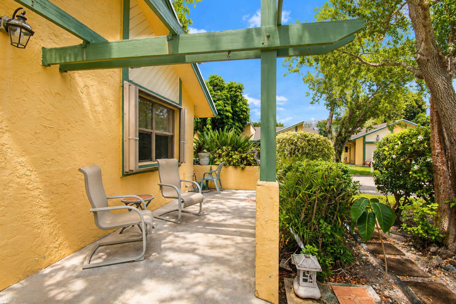 A yellow stucco house features a concrete patio with outdoor chairs and a wooden pergola — 7951 Little Lane, Boca Raton FL 33433, BOCA RATON, FL