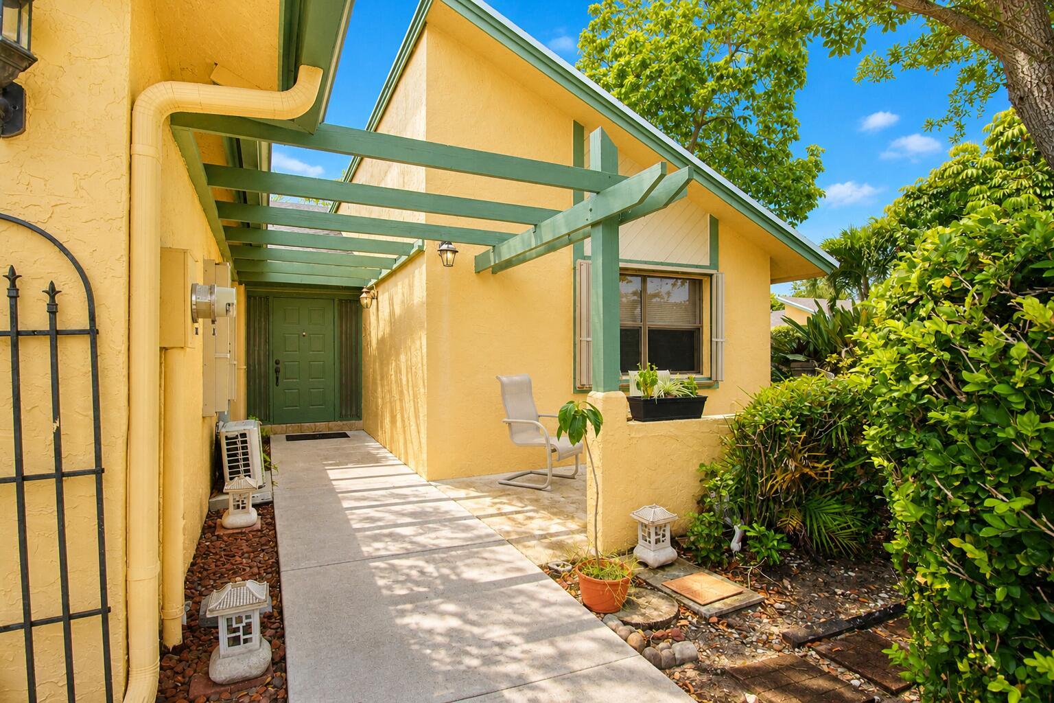 A yellow house exterior features a green pergola, a concrete walkway, and a green door — 7951 Little Lane, Boca Raton FL 33433, BOCA RATON, FL