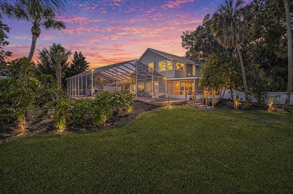 A two-story house with a screened-in pool enclosure sits on a grassy lawn at sunset — 3328 TOBERO LANE, SARASOTA, FL