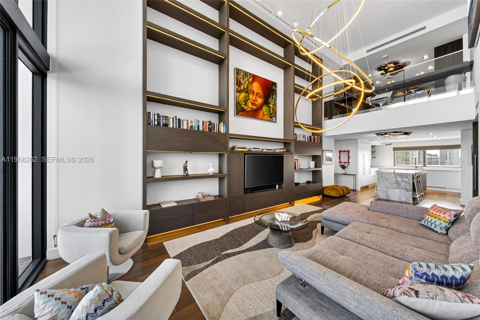 A modern living room features a double-height ceiling, a large built-in bookshelf, and a chandelier — 601 NE 36th St # 3407, Miami FL 33137, MIAMI, FL