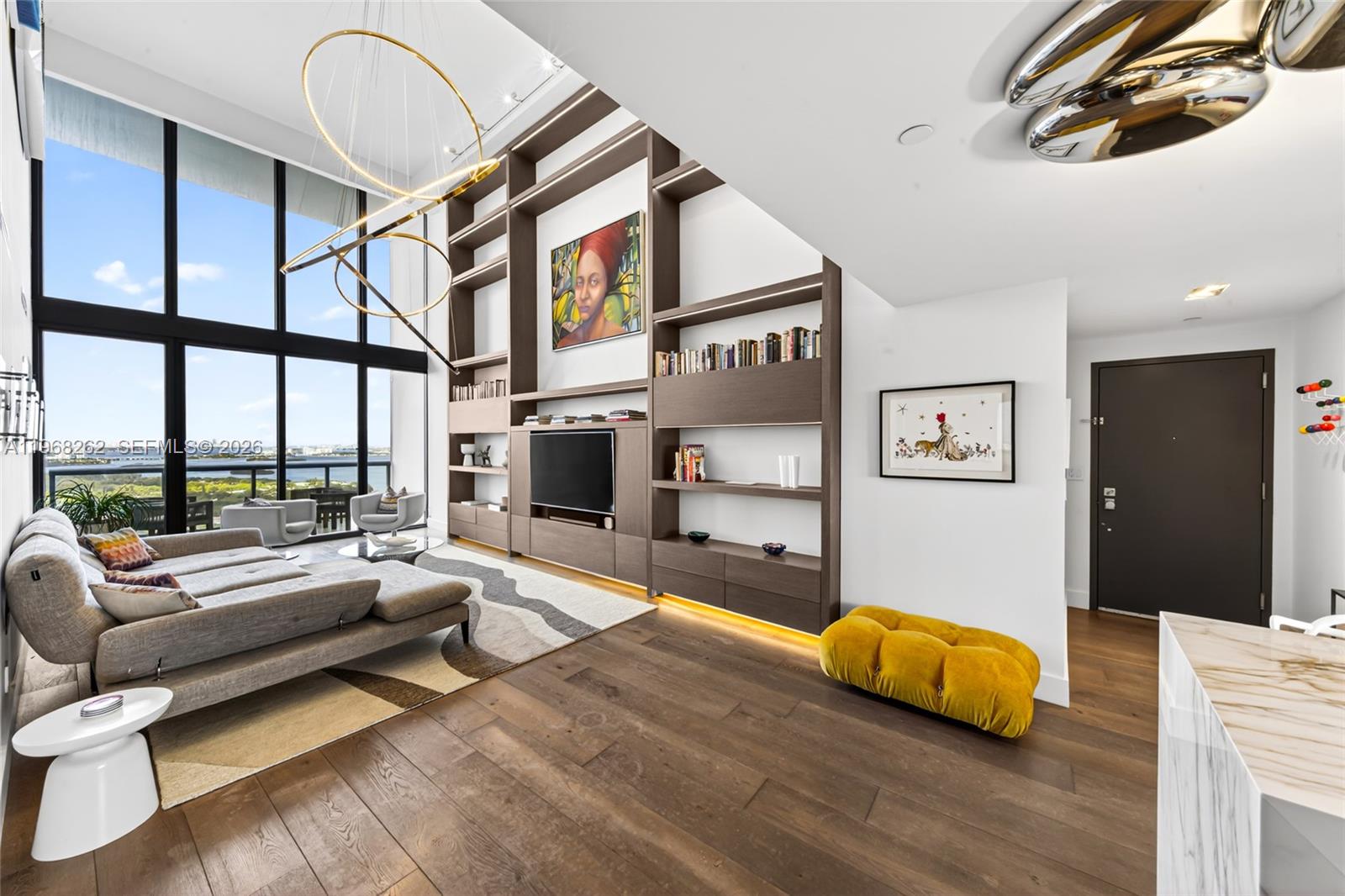 A modern living room features floor-to-ceiling windows, a large built-in shelving unit, and hardwood floors — 601 NE 36th St # 3407, Miami FL 33137, MIAMI, FL