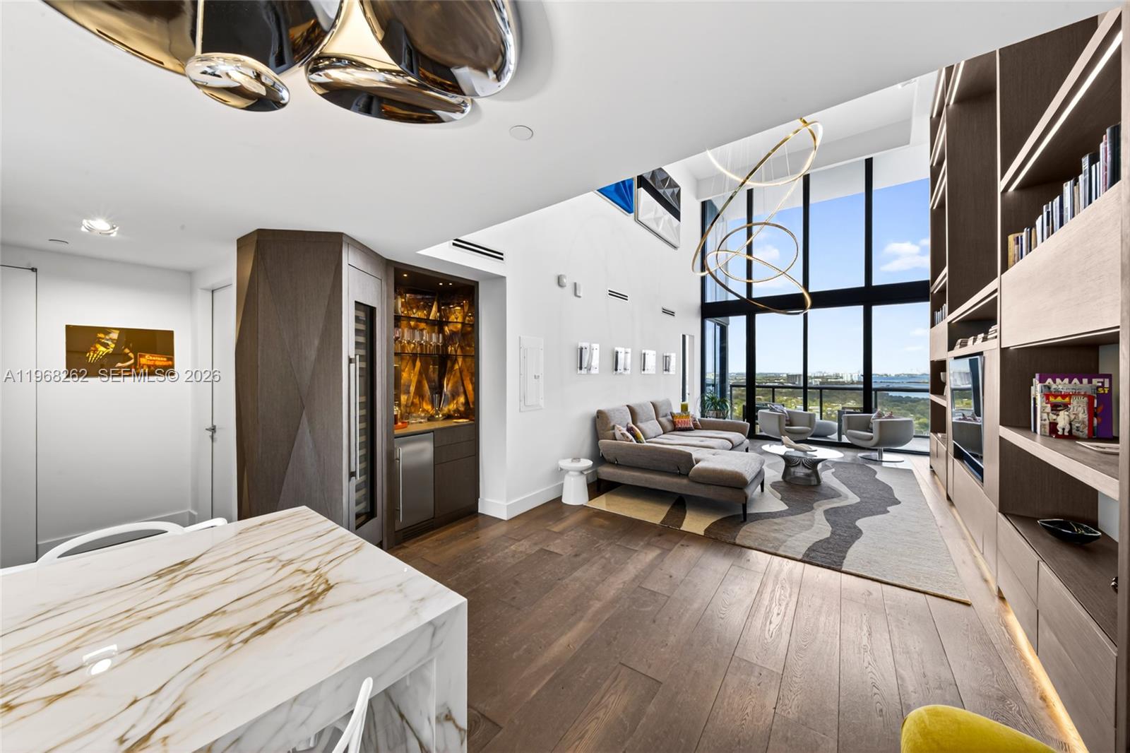 A modern living room features floor-to-ceiling windows, a built-in bar, and custom shelving — 601 NE 36th St # 3407, Miami FL 33137, MIAMI, FL