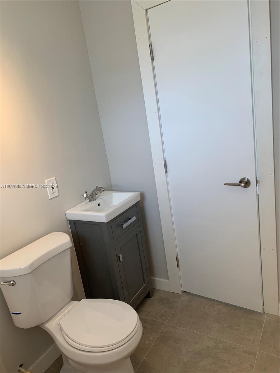 A small bathroom features a white toilet, a grey vanity with a sink, and a door — 2932 NW 16th Ave # 2B, Miami FL 33142, MIAMI, FL