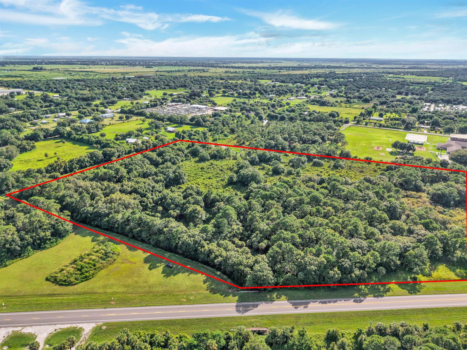 An aerial view shows a rectangular, wooded plot of land outlined in red beside a road — 100 NW 38th Avenue, Okeechobee FL 34972, OKEECHOBEE, FL