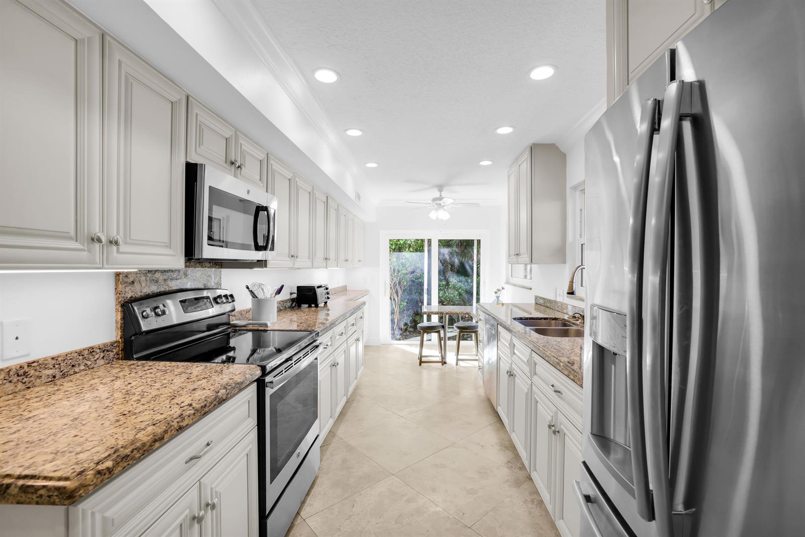 A galley kitchen features light-colored cabinets, granite countertops, stainless steel appliances, and tile flooring — 4161 U.s. Hwy 1 # I2, Jupiter FL 33477, JUPITER, FL