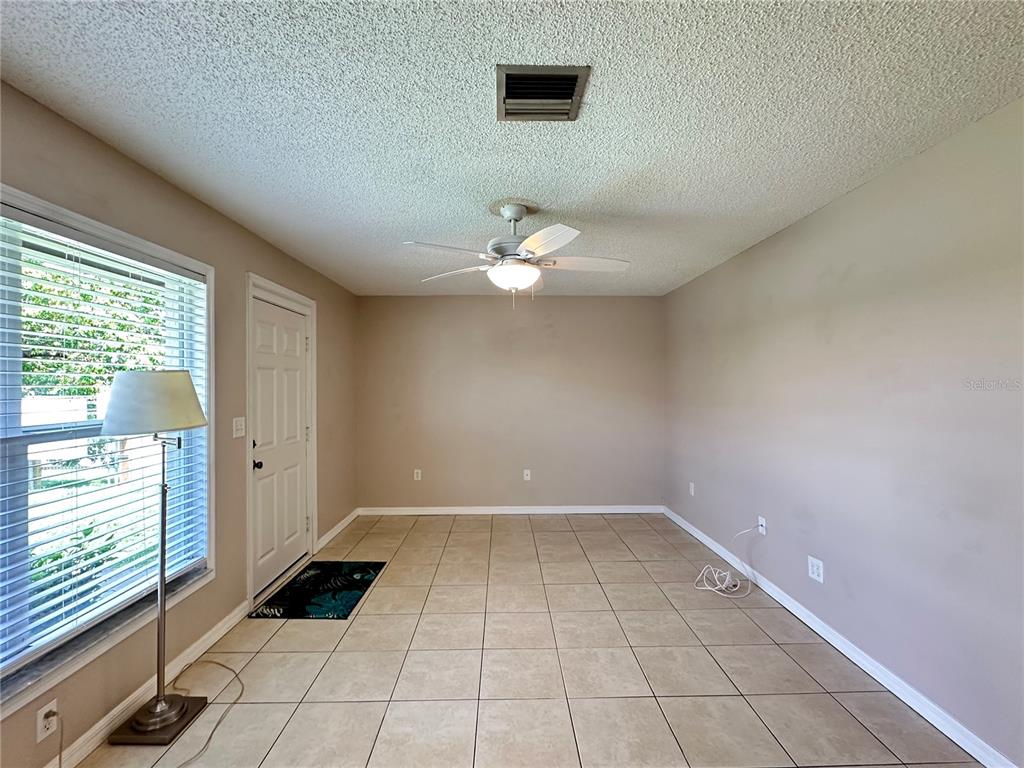 An empty room features beige walls, tile flooring, a ceiling fan, and a front door — 21150 GERTRUDE AVENUE UNIT N3, PORT CHARLOTTE, FL