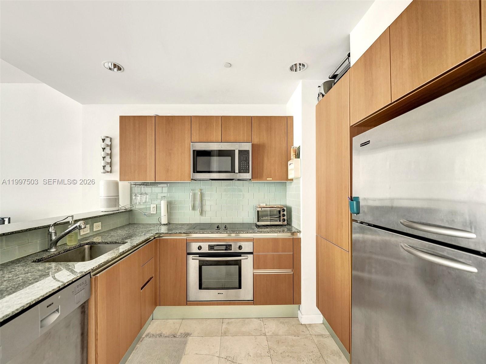 A kitchen features wood cabinets, stainless steel appliances, granite countertops, and a light green backsplash — 1050 Brickell Ave # 2722, Miami FL 33131, MIAMI, FL