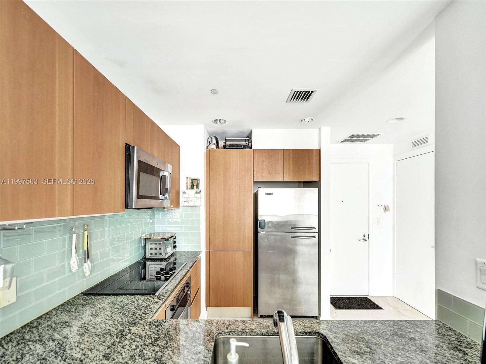 A kitchen features light wood cabinets, granite countertops, a stainless steel refrigerator, and light-blue backsplash — 1050 Brickell Ave # 2722, Miami FL 33131, MIAMI, FL