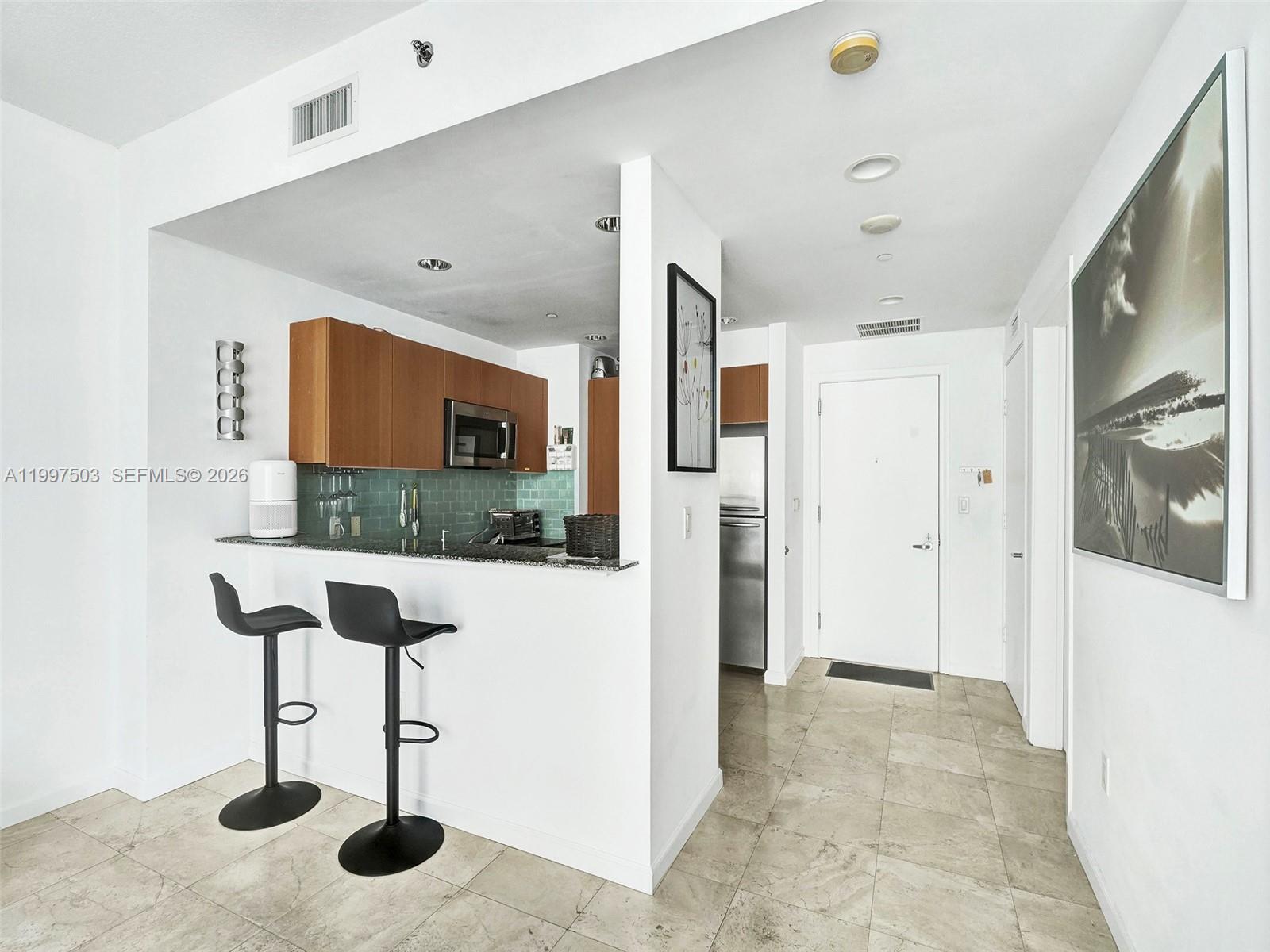 A kitchen with wood cabinets and a breakfast bar overlooks a tiled entryway — 1050 Brickell Ave # 2722, Miami FL 33131, MIAMI, FL