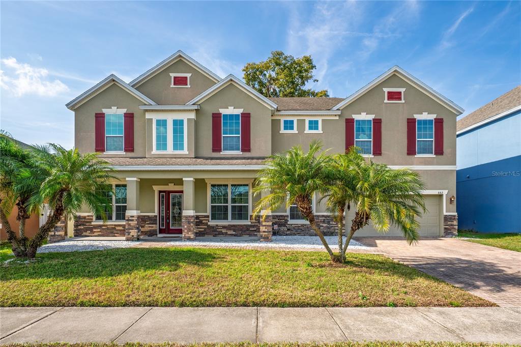 A two-story suburban house features a tan stucco facade, stone accents, and red window shutters — 882 COUNTS CREST CIRCLE, APOPKA, FL