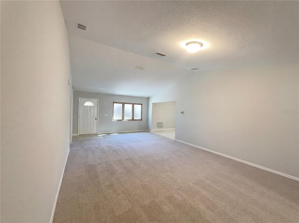 A spacious living room features neutral carpeting, light gray walls, and a vaulted ceiling — 13824 SW 114TH CIRCLE, DUNNELLON, FL