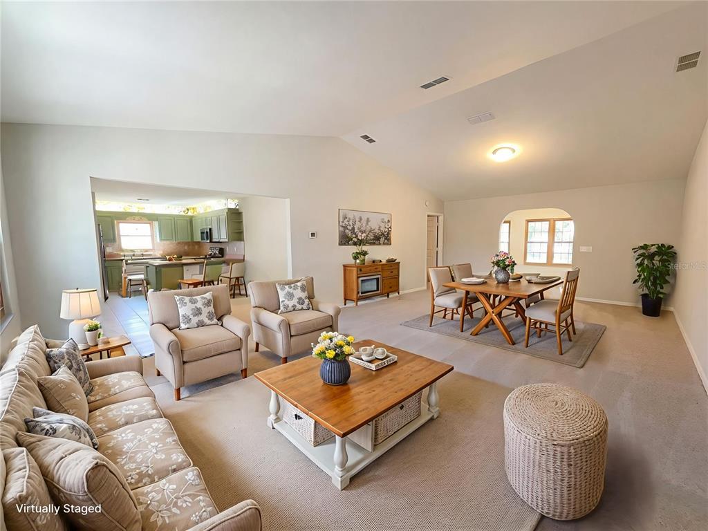 A living room with vaulted ceilings, beige carpeting, and an adjacent kitchen and dining area — 13824 SW 114TH CIRCLE, DUNNELLON, FL