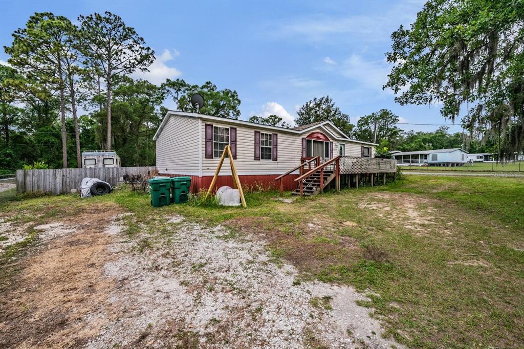 A single-story manufactured home with a wooden deck and gravel driveway under a blue sky — 5074 N DEWEY WAY, HERNANDO, FL