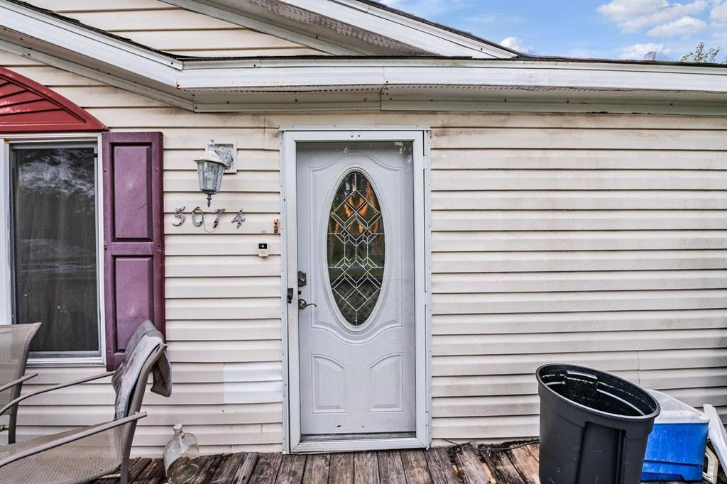 A white front door with an oval glass insert sits on a wooden porch — 5074 N DEWEY WAY, HERNANDO, FL