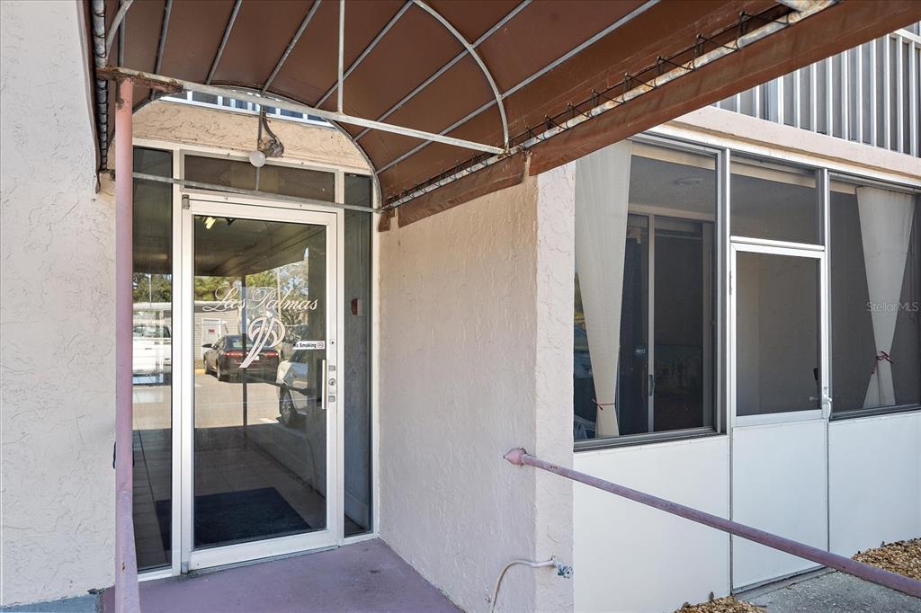 The exterior entrance of a building features a glass door under a metal awning — 519 ALBEE FARM ROAD UNIT 111, VENICE, FL